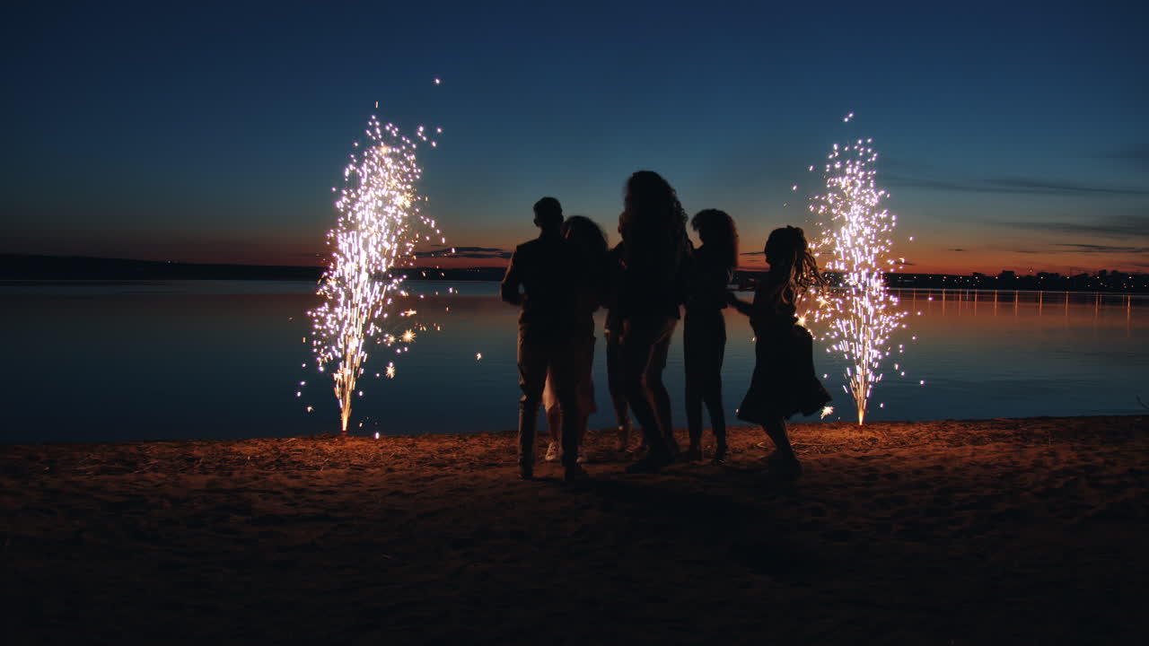Friends Dancing on a Beach at Sunset with Fireworks