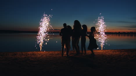 friends dancing on a beach at sunset with fireworks