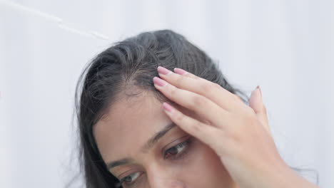 a young lady applying minoxidil with a dropper on hair root and massaging scalp to improve hair growth.