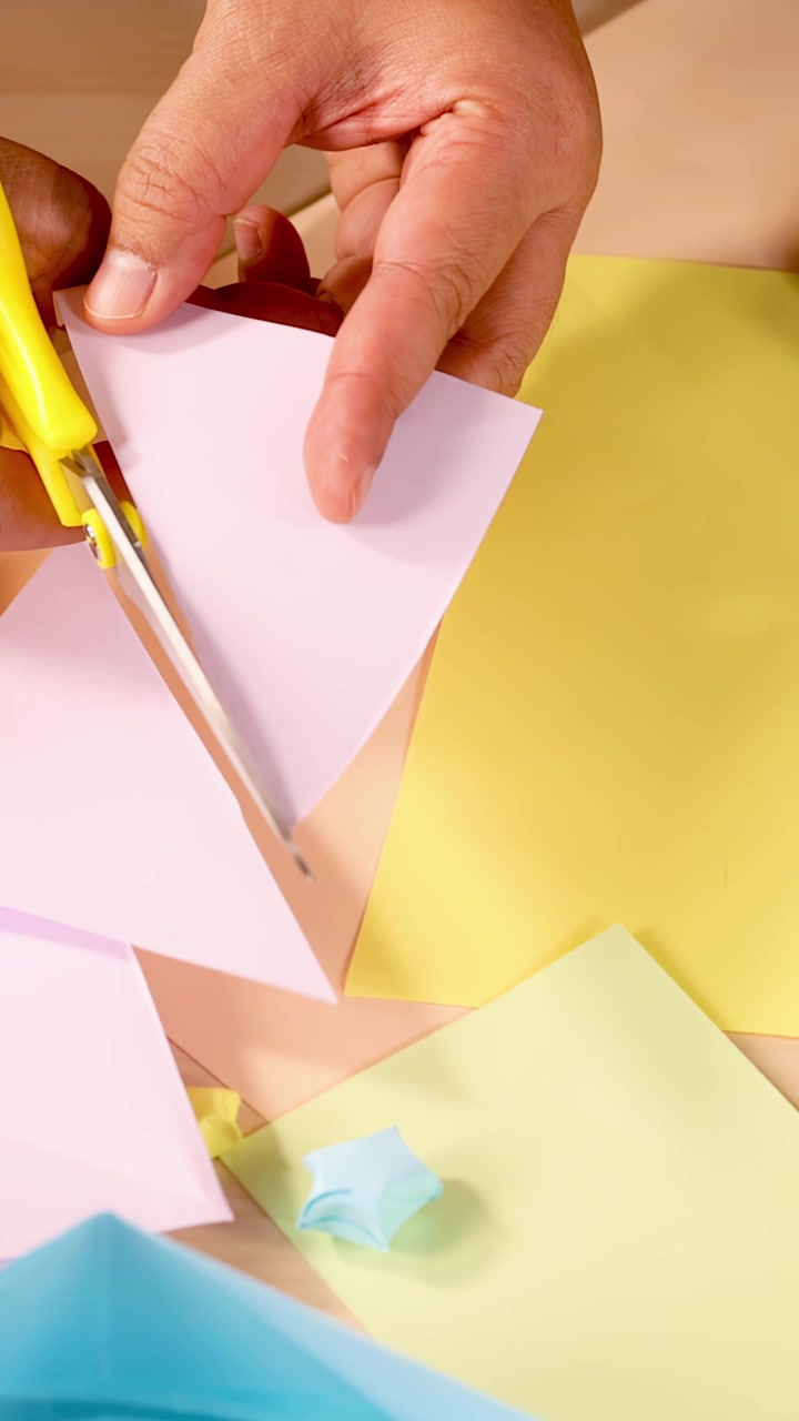 Mani tagliano e piegano carta colorata in forme di origami su un piano di lavoro ben illuminato