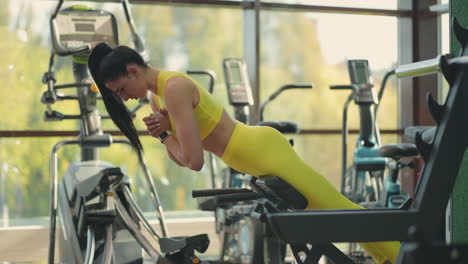 young beautiful hispanic woman performs hyperextension in the gym. the determined woman performs the back extension at the bench in the gym. intense masculine energy. healthy lifestyle. sport concept