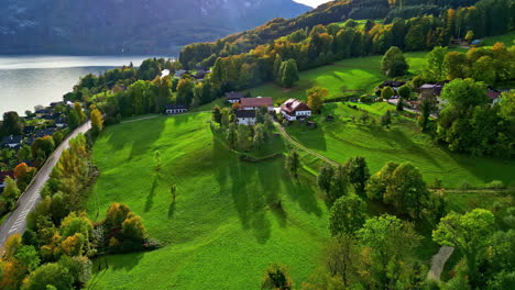 a rustic green landscape of a village located on a hill near a lake with colourful trees