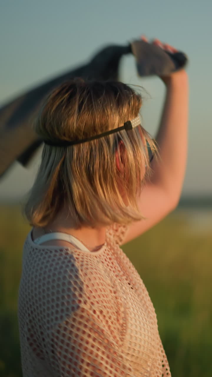 한 젊은 여성이 해가 지는 동안 잔디에서 춤을 추면서 기쁜 마음으로 천을 공중에 흔들고 있다.