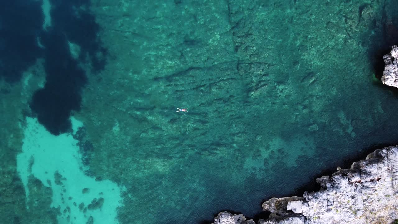 아드리아 해, 바위 바닥 및 해안의 파란색 얕은 잔잔한 물에서 수영하는 남자, 위에서 아래로