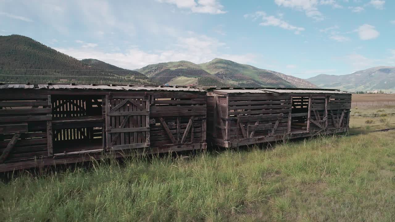 vista de drones de un tren de madera abandonado en el campo de colorado con montañas verdes en el fondo
