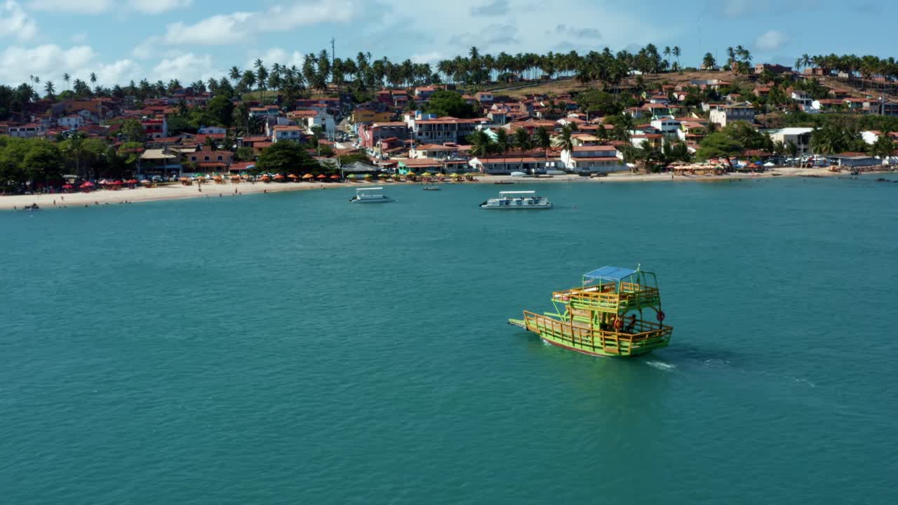 toma aérea de un dron después de un pequeño y colorido barco de transporte que navega en un gran río turquesa tropical desde la playa de restinga hasta la playa de barra do cunhaú en río grande do norte, brasil