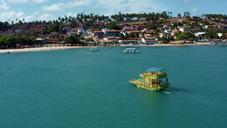 Aerial-drone-shot-following-a-small-colorful-transport-boat-sailing-on-a-large-tropical-turquoise-river-from-the-Restinga-beach-to-the-Barra-do-Cunhaú-beach-in-Rio-Grande-do-Norte,-Brazil