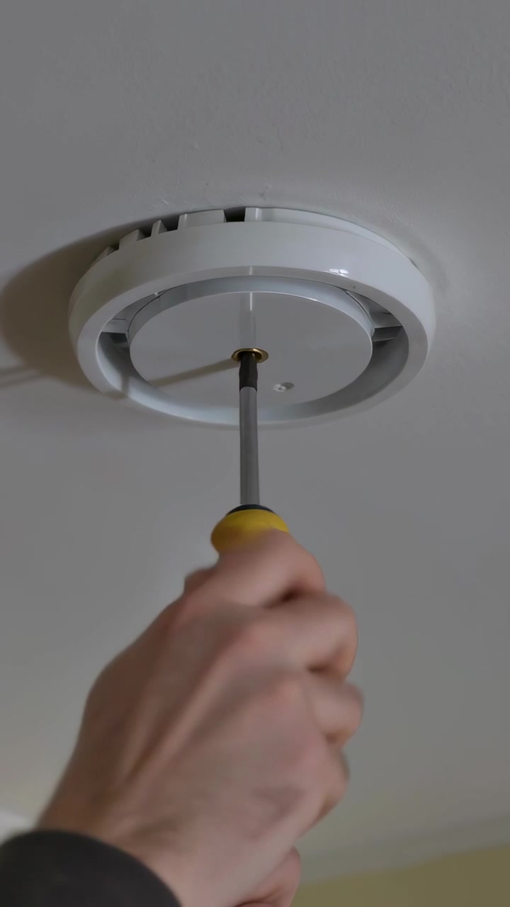 Vertical video: Turning arm tightening center screw home ceiling yellow driver darksleeve lighting