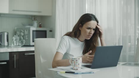 Mujer-Enojada-Escribiendo-En-Una-Computadora-Portátil-En-La-Cocina.-Mujer-Preocupada-Trabajando-En-Línea