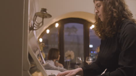 krullende vrouw die piano speelt in een restaurant en een bladmuziek weggooit