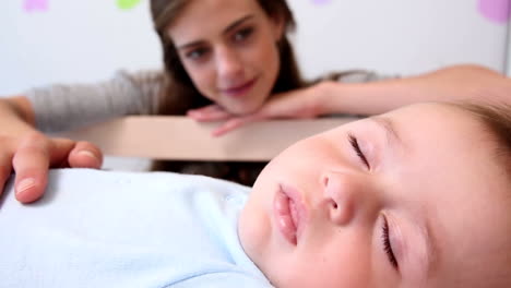 happy mother watching over baby son in crib