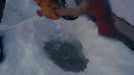 man is holding an axe making a hole in a frozen lake