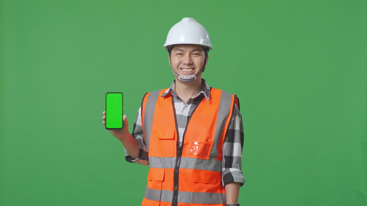 Asian Male Engineer With Safety Helmet Smiling And Showing Green Screen Smartphone To The Camera While Standing In The Green Screen Background Studio