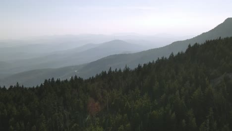 revealing-far-away-winding-road-behind-a-mountain-covered-with-evergreen-trees-and-layers-of-hills-in-the-background