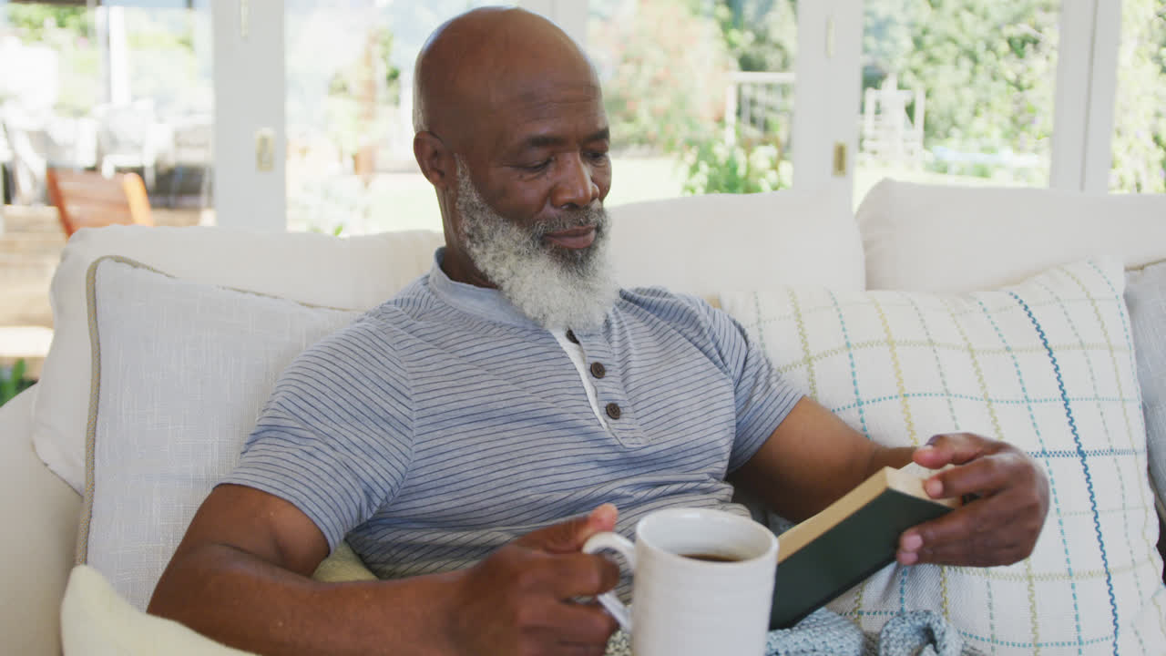 Senior african american man reading book and holding mug of tea