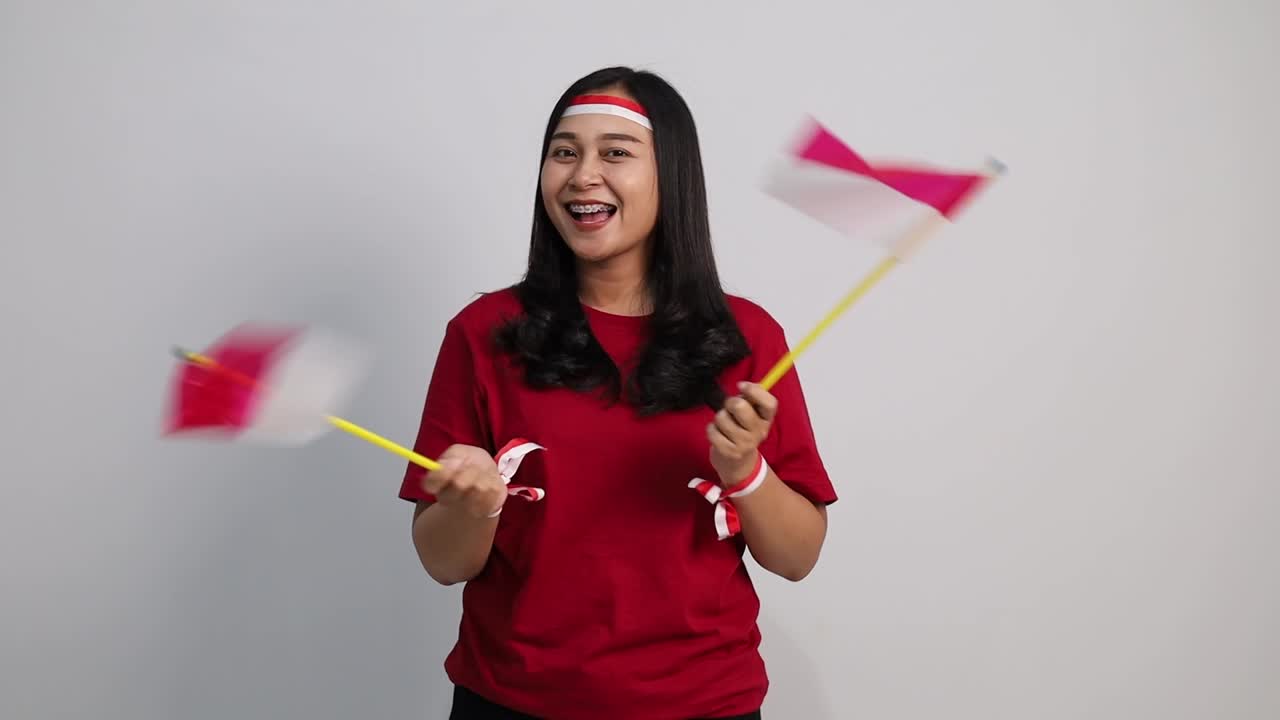 Donna indonesiana allegra in piedi che tiene la bandiera rossa e bianca per celebrare il giorno dell'indipendenza dell'Indonesia.