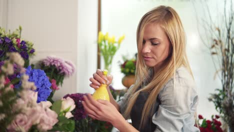 Slow-Motion-shot-of-young-attractive-blonde-female-florist-spraying-water-on-bunch-of-flowers-in-flower-shot
