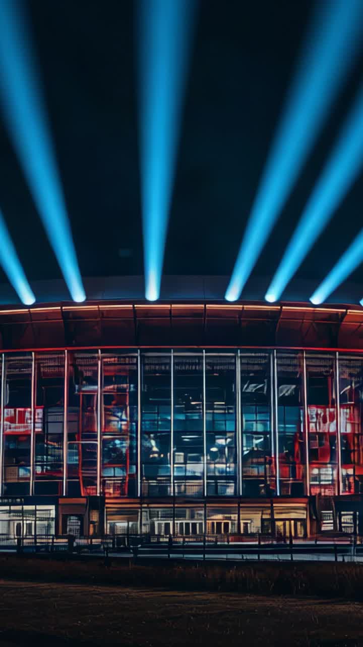 Vertical video: Powering six spotlights casting blue-white beams on arena facade with red LED