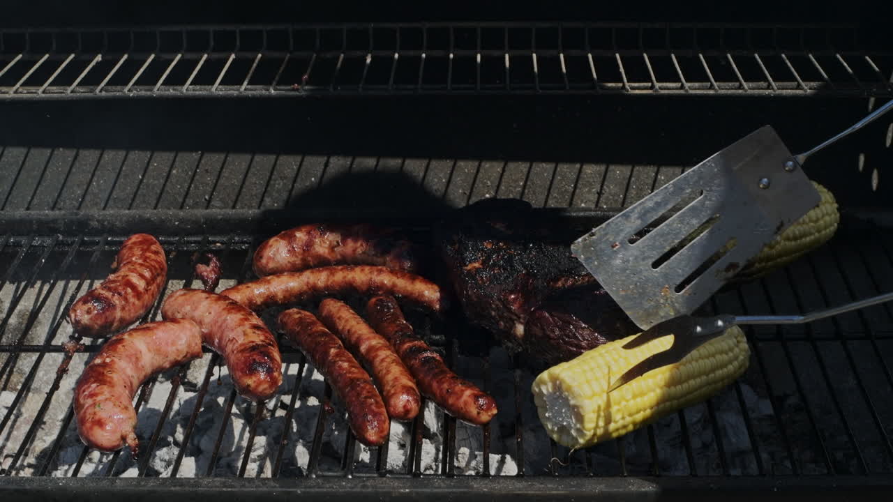 Barbecuing some sausages, corn and steak for a good summer outdoor al fresco meal on the bbq - mid shot