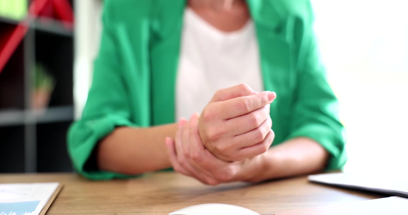 Vrouw in groene jas houdt haar pols vast en voelt ongemak en pijn