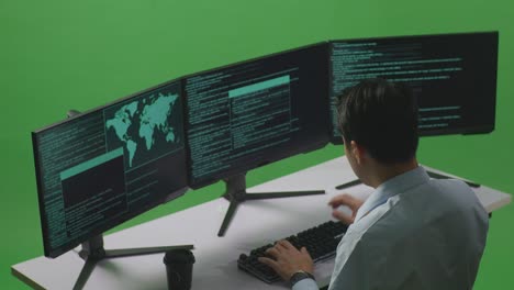 vista lateral de un desarrollador asiático feliz celebrando mientras escribe código con múltiples pantallas de computadora en el estudio de pantalla verde