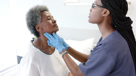 médica afroamericana probando el cuello de una paciente anciana en una habitación del hospital, en cámara lenta