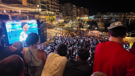 large crowd watching a football match on a big screen at night