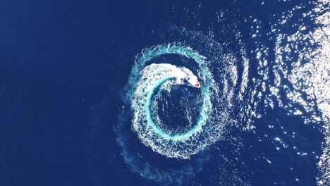 top down drone shot of motor boat making wake circles in blue sea water, high angle aerial view