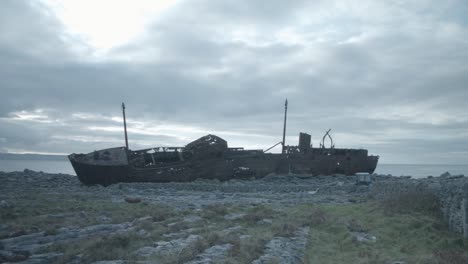Shipwreck-dilapidated-on-rocky-shoreline,-SIDE-HULL-SHOT