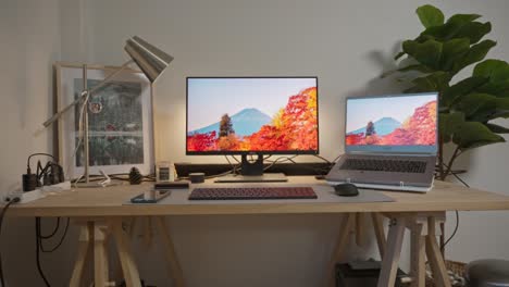 espacio de trabajo con portátil moderno, pantalla de visualización, lámpara, marco de imágenes en escritorio de madera y árbol artificial en una habitación de estudio minimalista