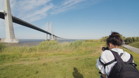 young woman captures a moment and takes a photo of the scenery. urban and nature. female photographer takes a photo of vasco da gama bridge