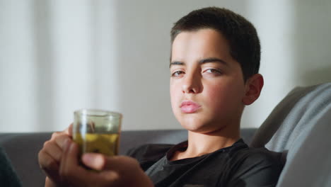 boy with tea cup staring at camera, holding cup close to his mouth while looking tired and sick, with sunlight reflecting off his face, creating a soft, warm ambiance