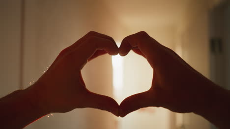 pov of hands forming a heart shape against the home's bright sun rays, creating a warm, loving silhouette