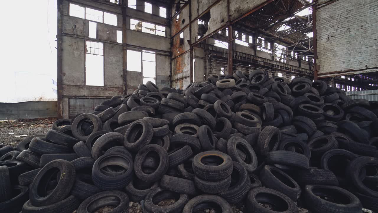Big bunch of old tires on the background of a ruined plant. Pile of used tires lays on a dirty floor.