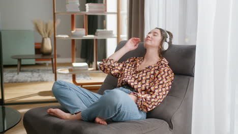 Girl-relaxing-on-lounge-chair-meditates-or-listens-to-podcast-on-headphones