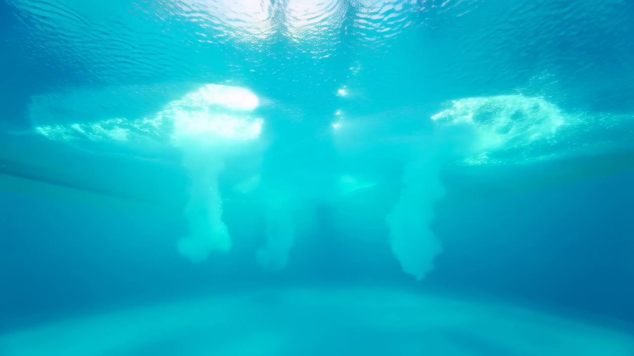 從下方看明亮的藍色游泳池，泳客在水面附近以黑色剪影移動，強烈陽光造成眩光和反射。