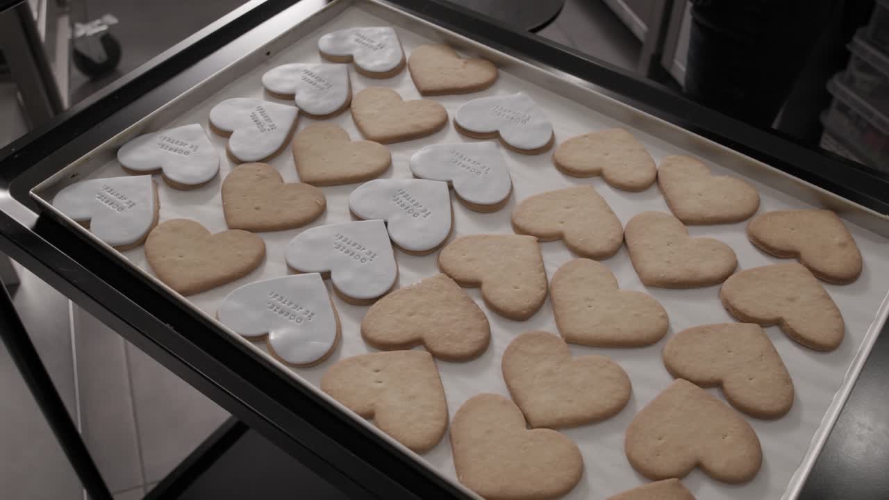 Woman arranges freshly baked butter cookies in the shape of hearts on a baking tray in a pastry shop, 4K