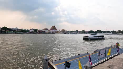a riverboat glides along the chao phraya river in bangkok, thailand, under a partly cloudy sky, showcasing vibrant cityscapes