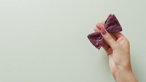 video of hand of caucasian woman holding red and black bow tie over grey background