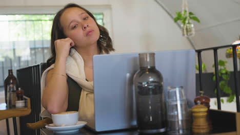 slow motion shot of a female putting in her earphones and drinking her coffee at her laptop