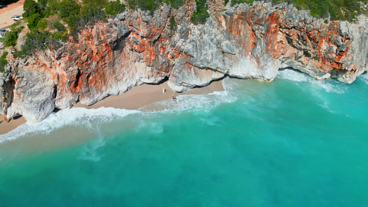 Ripresa aerea con drone in avanzamento sopra ripide scogliere rocciose lungo la spiaggia di Gjipe, Albania, in una giornata di sole.