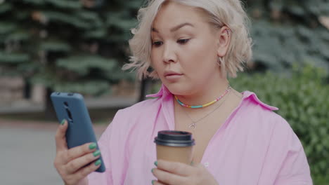 woman using phone outdoors with coffee