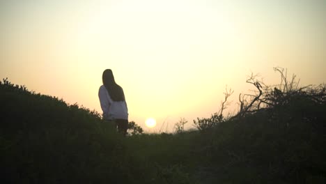 Wide-shot-of-a-girl-walking-through-nature-during-sunset