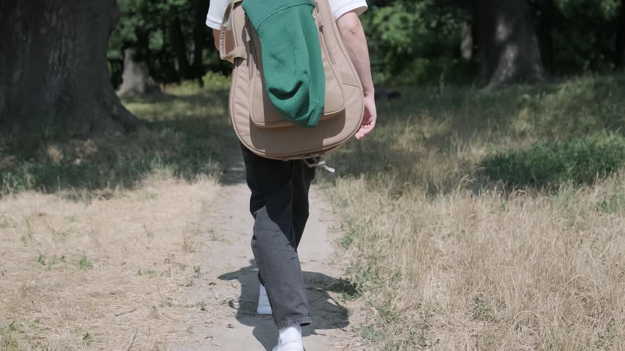 숲 근처의 거리에서 기타를 들고 는 젊은 남자