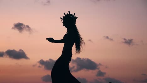 Side view of sexy, elegant and erotic arabian woman performing belly dance on the beach during golden hour. Silhouette. Slow motion