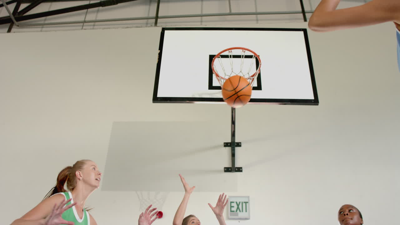 Playing basketball, women reaching for ball near hoop in indoor court