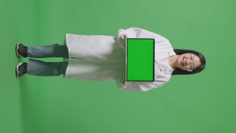 cuerpo lleno de mujer científica asiática sonriendo y mostrando pantalla verde portátil a la cámara mientras está de pie en el fondo de la pantalla verde en el laboratorio