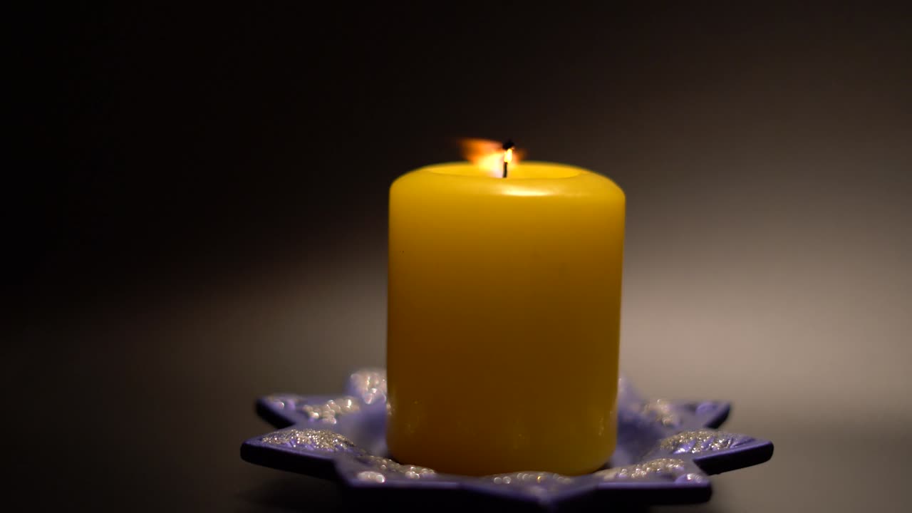 Velká žlutá svíčka a slavnostní stojan na černém pozadí. Světlo bylo tlumené. Svíčka je zapálena zápalkou