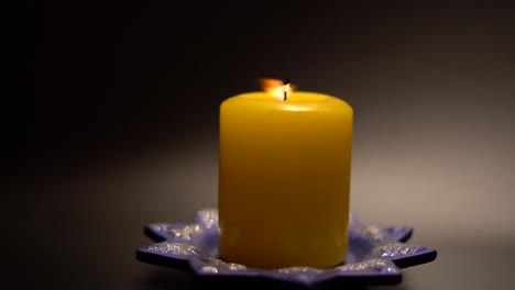 a large yellow candle and a festive stand on a black background. the light was dim. the candle is lit with a match.