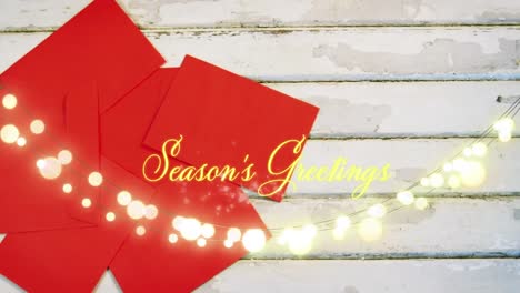 Animation-of-text,-season's-greetings,-in-yellow,-over-string-lights-and-red-envelopes